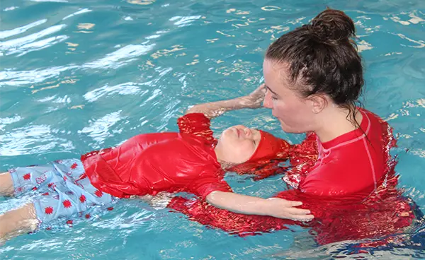 swim instructor with small boy floating on back in pool